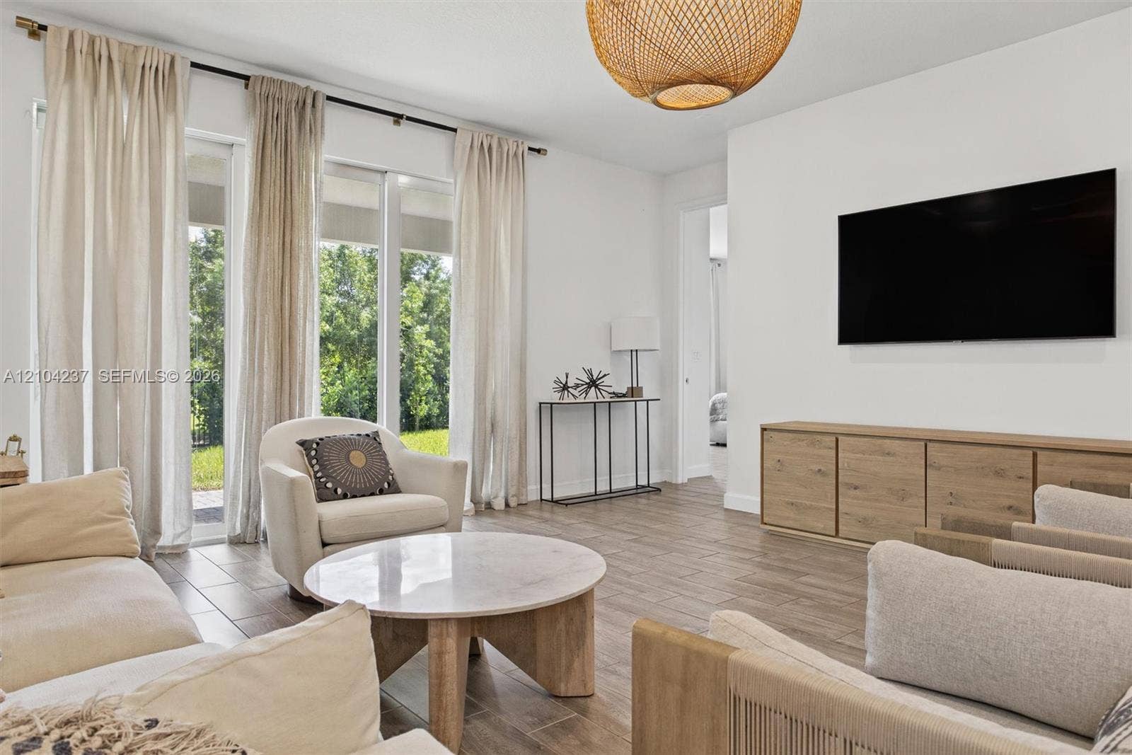 Living area featuring wood-finish flooring, floor-to-ceiling sliding glass doors, and a decorative woven drum pendant light