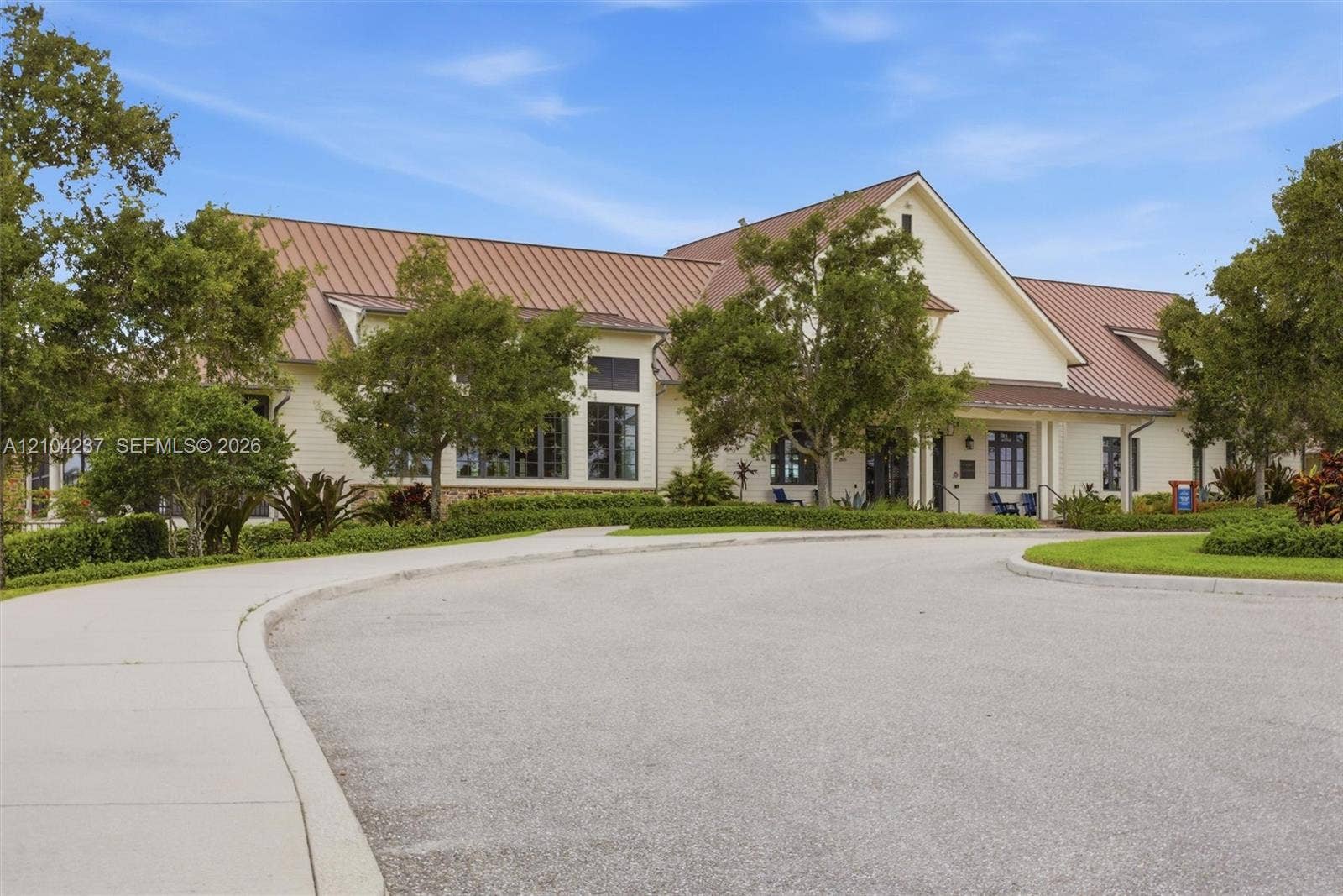 Single-story exterior featuring light-toned horizontal lap siding, a standing seam metal roof, multi-pane windows, and a paved circular driveway