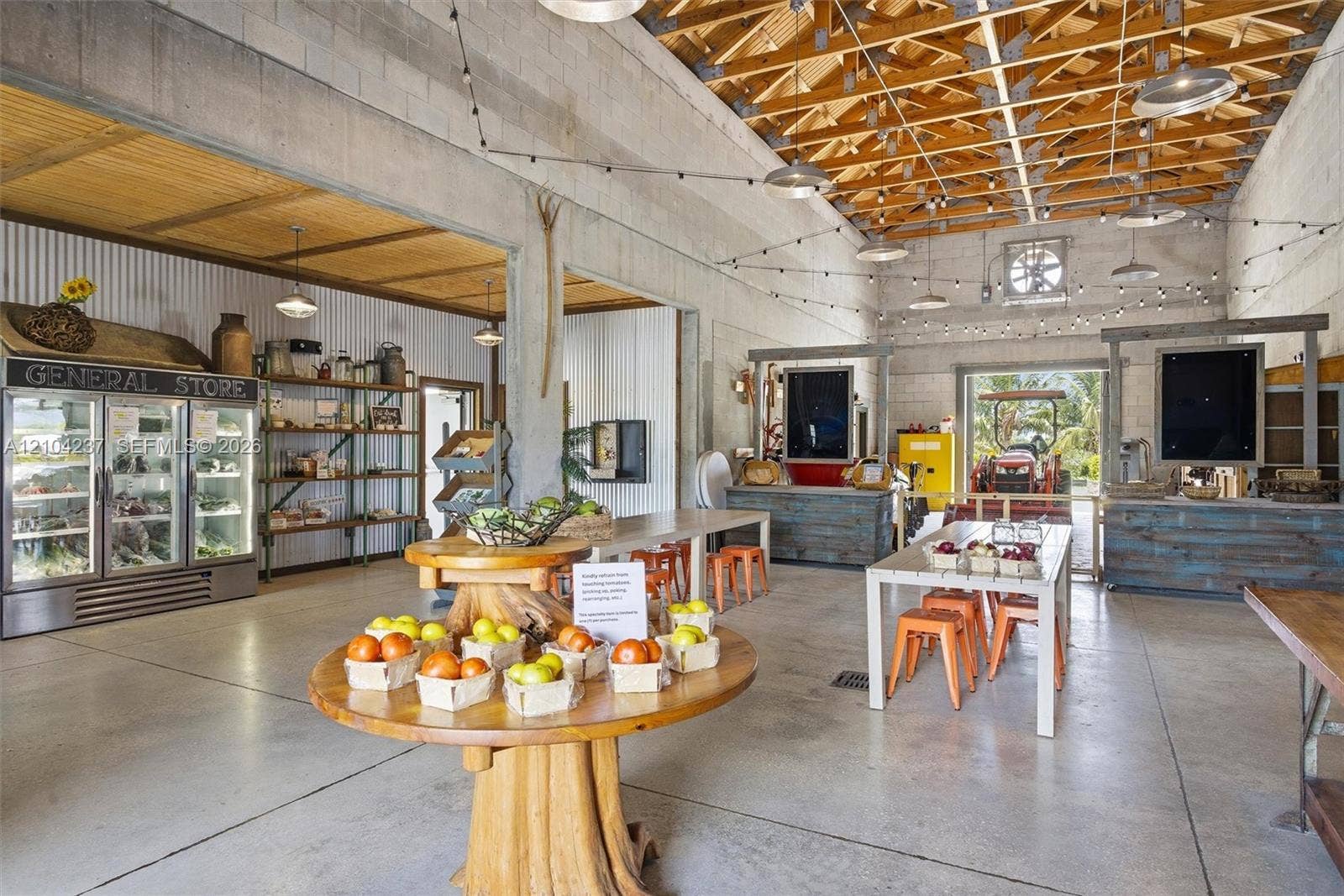 Open-concept industrial space featuring exposed wood truss ceilings, polished concrete flooring, corrugated metal wall paneling, and integrated string lighting
