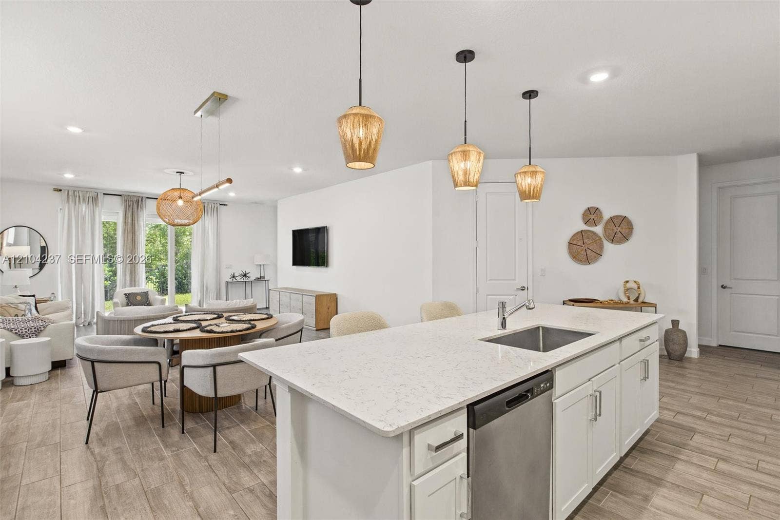 Kitchen island featuring stone-finish countertops, stainless steel undermount sink, shaker-style cabinetry, wood-finish flooring, and multi-pendant lighting