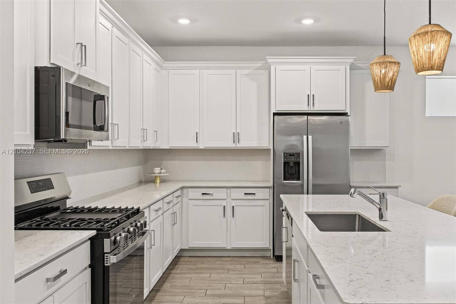 Kitchen featuring white shaker-style cabinetry, quartz countertops, a central island with an undermount stainless steel sink, stainless steel appliances, and wood-finish tile flooring