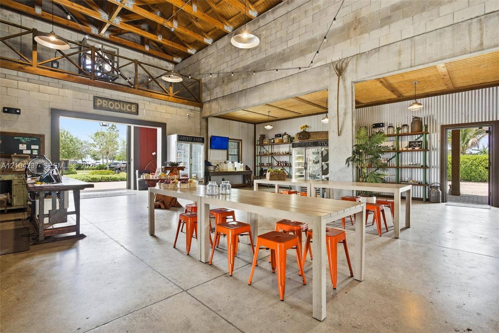 Industrial-modern open-concept living space featuring polished concrete flooring, exposed wood beam ceiling, and abundant natural light from expansive glass doors and windows