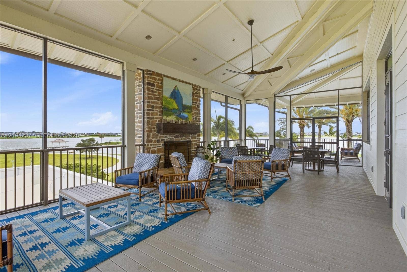 Expansive screened porch with wood-finish flooring, ceiling fan, and brick fireplace with stone surround