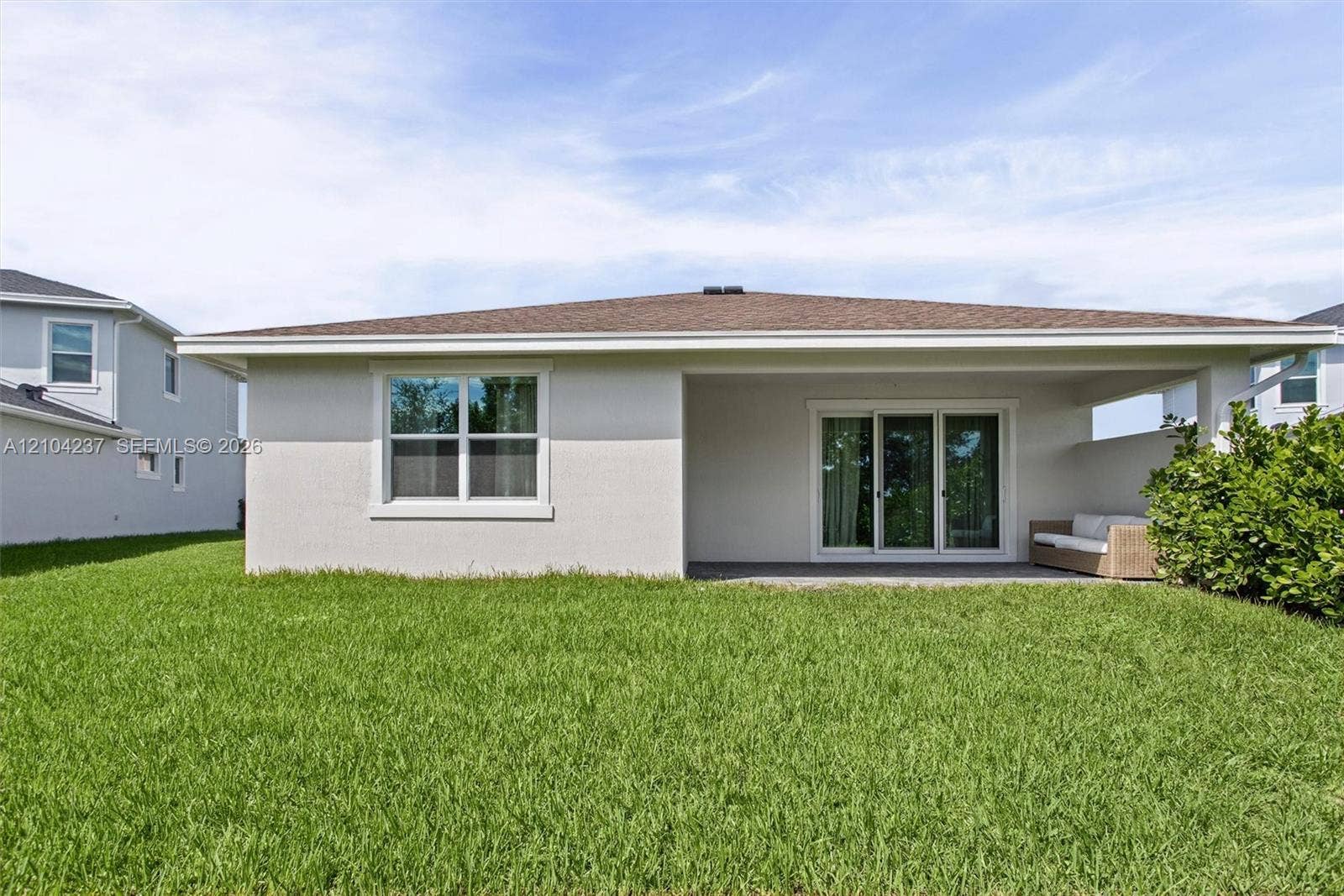 Stucco exterior featuring a covered patio, sliding glass doors, and a manicured lawn