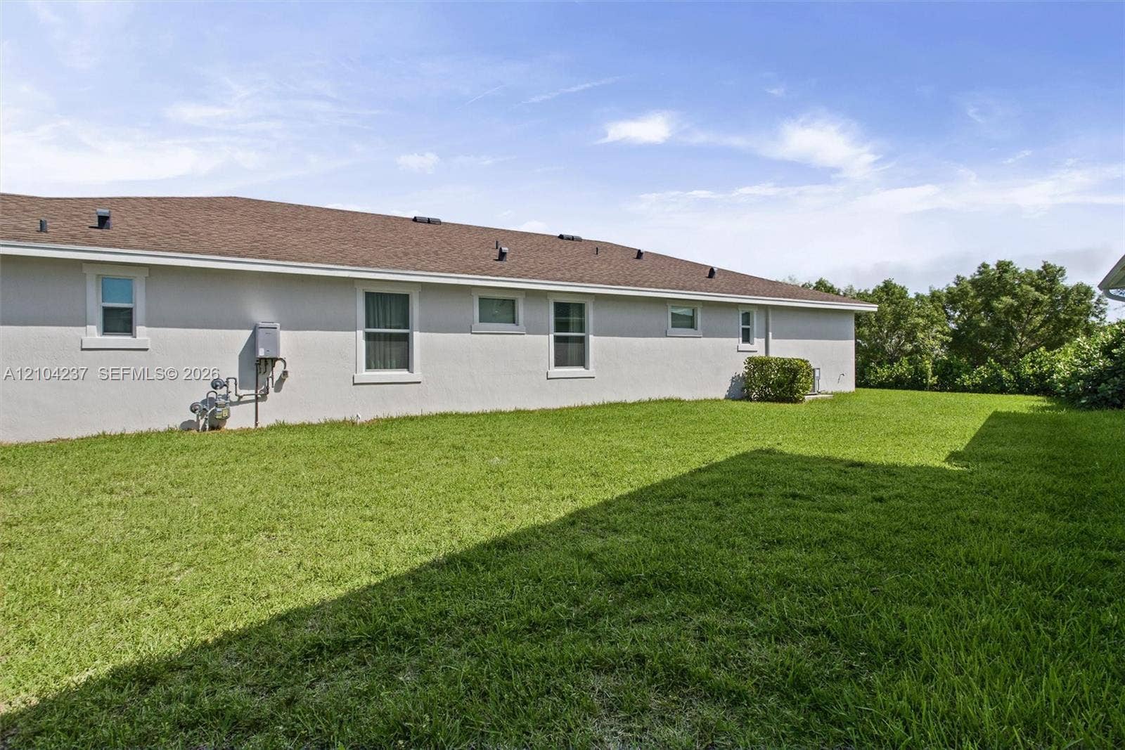 Stucco exterior featuring a pitched shingle roof, multiple windows, and an expansive grass lawn