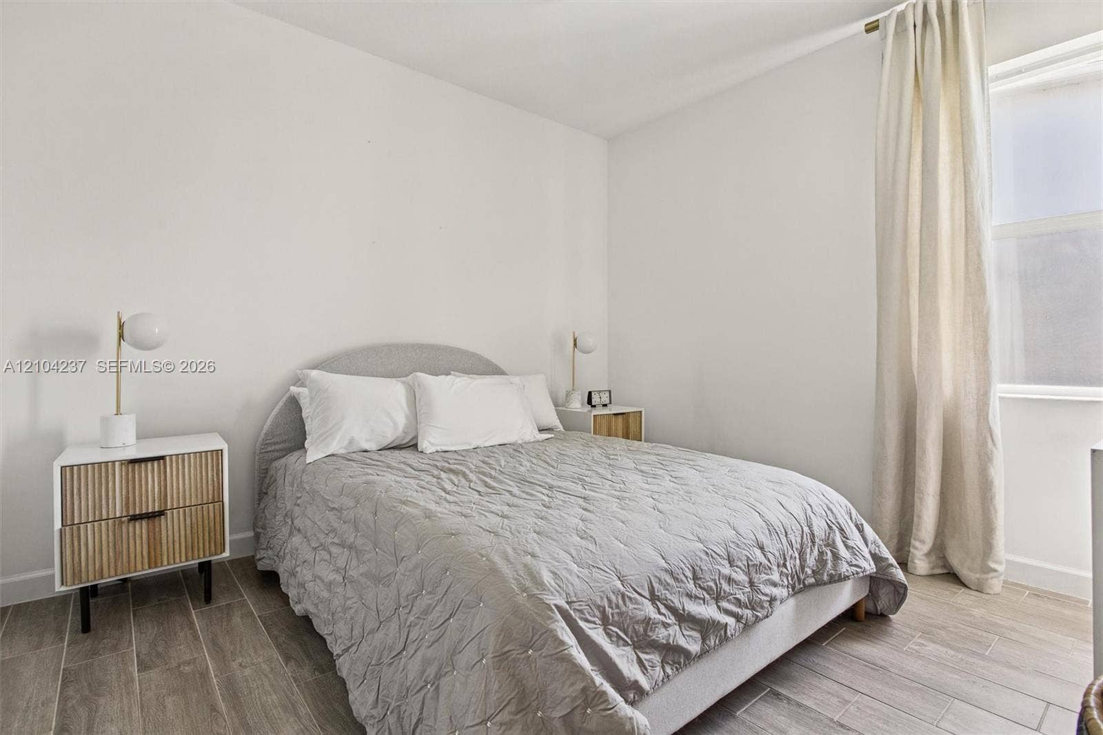 Neutral-toned interior featuring wood-finish tile flooring, clean-lined walls, and a recessed window with full-length drapery