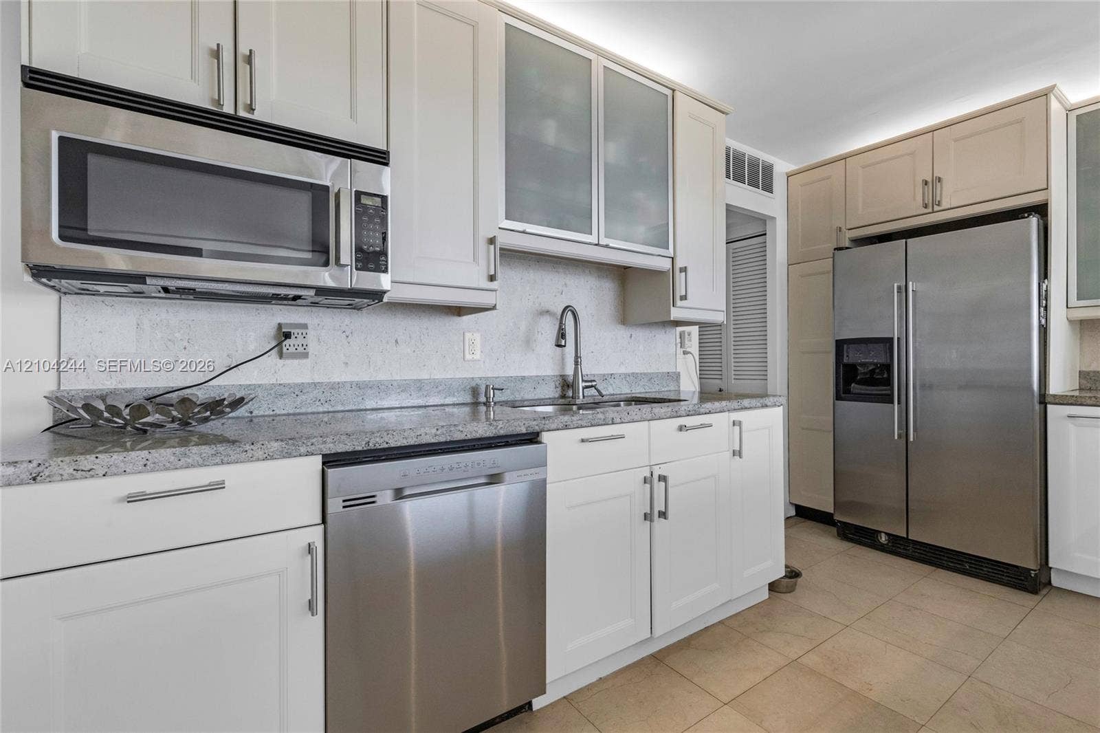 Kitchen featuring light-toned cabinetry with glass-fronted uppers, stone-finish countertops, stainless steel appliances, and tile flooring