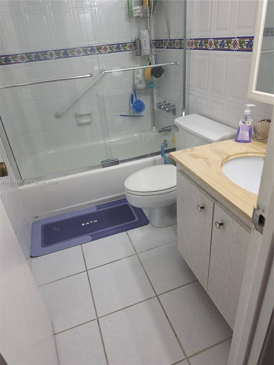 Bathroom featuring a vanity with a countertop, tiled walls with a decorative accent border, a shower-tub combination with sliding glass doors, and tiled flooring