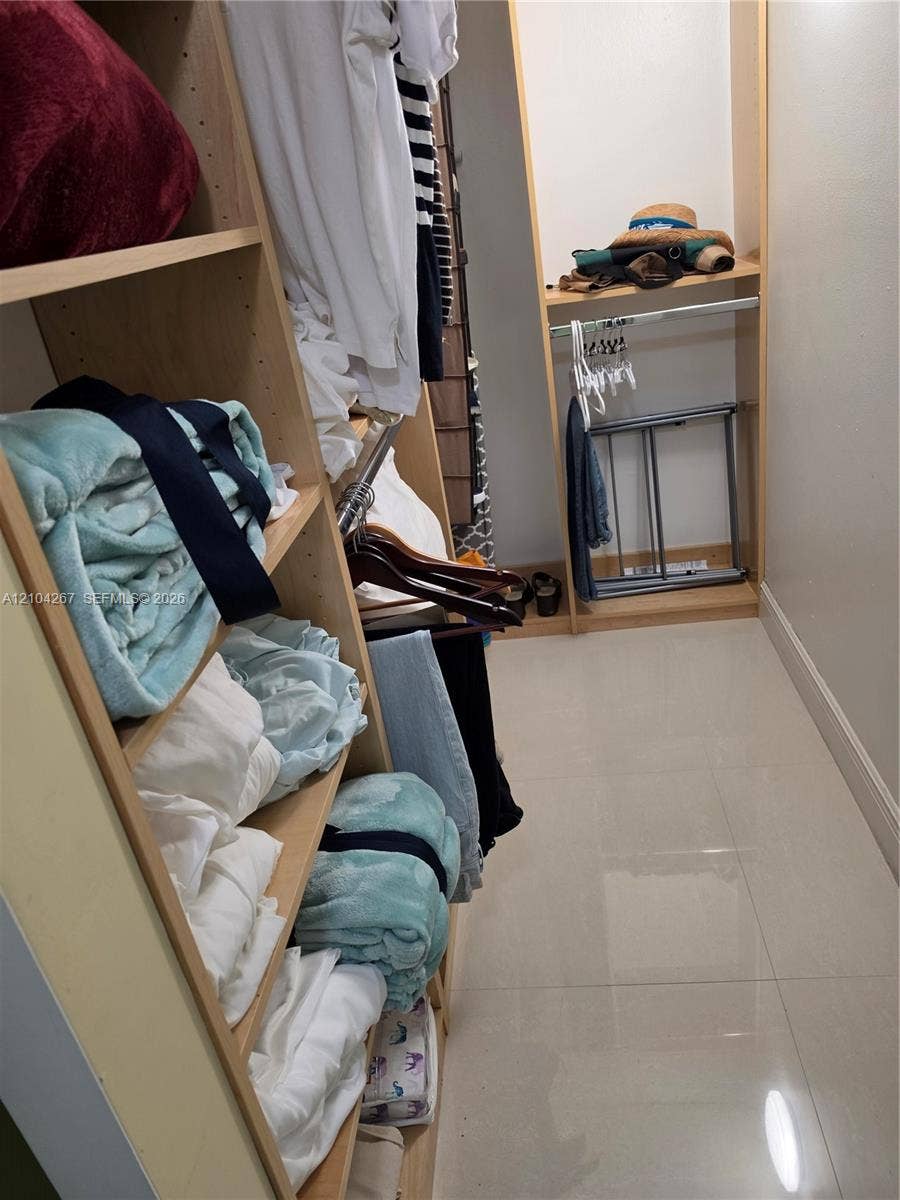 Walk-in closet featuring light-toned custom shelving, integrated storage cubbies, and large-format tile flooring