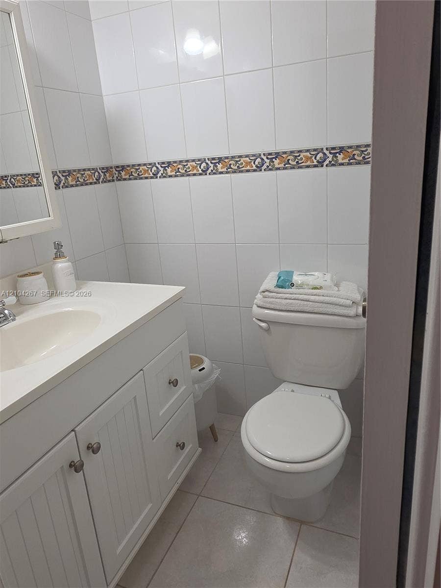 White cabinetry vanity with a solid-surface countertop and integrated sink, complemented by neutral tile flooring and full-height wall tiling featuring a decorative accent border