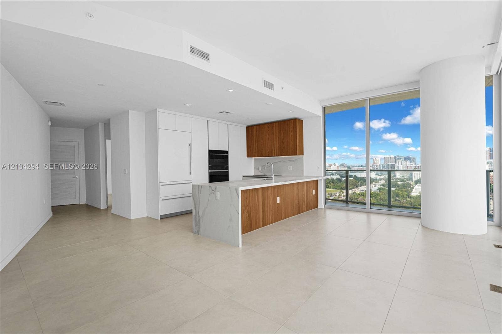 1400 Biscayne Boulevard, #1606, Miami, FL 33132 Open concept living area with light-toned tile flooring, floor-to-ceiling windows, and a modern kitchen featuring wood-finish cabinetry, integrated appliances, and a waterfall island