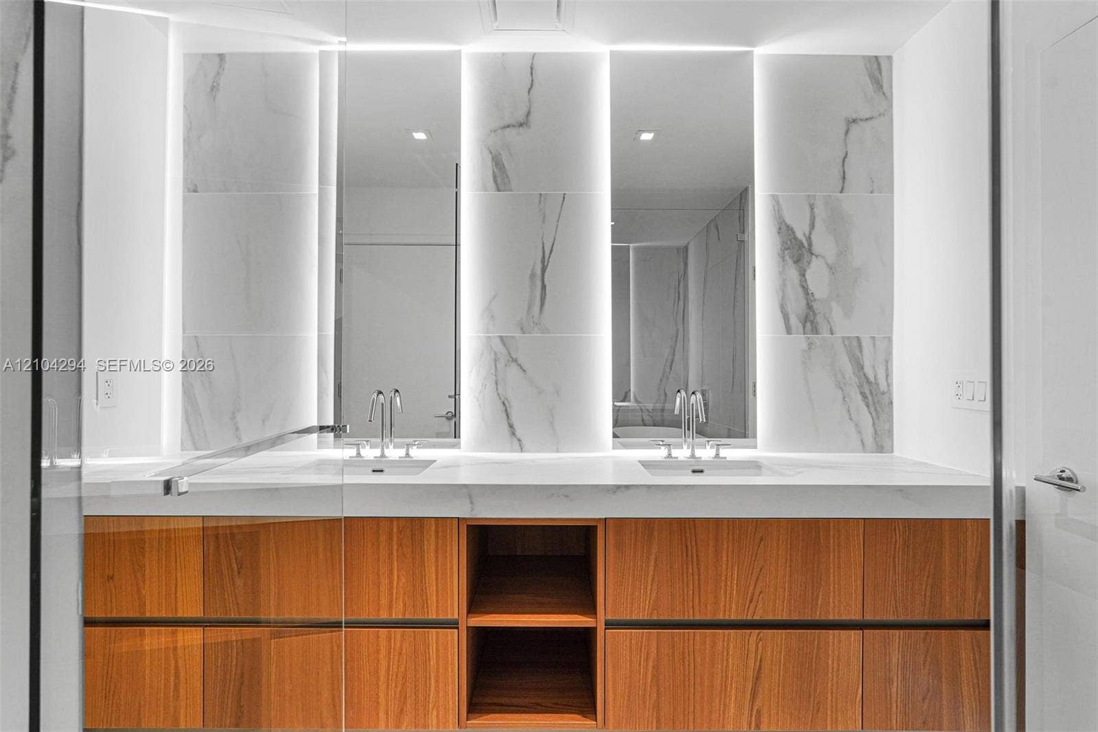 1400 Biscayne Boulevard, #1606, Miami, FL 33132 Dual vanity featuring wood-finish cabinetry, integrated sinks, a solid surface countertop, and backlit mirrors with wall-mounted stone-look tiles
