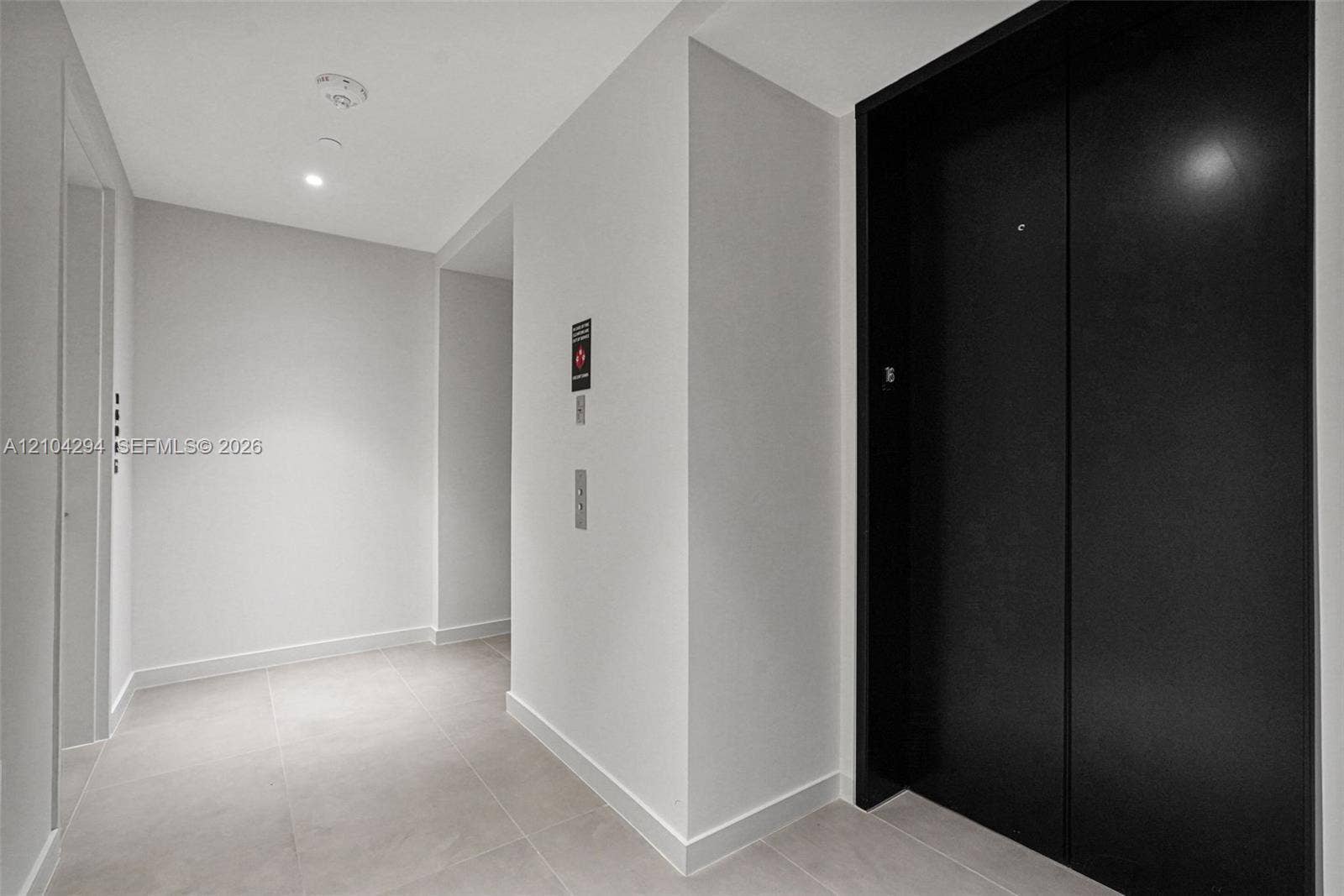 1400 Biscayne Boulevard, #1606, Miami, FL 33132 Recessed ceiling lighting illuminates the corridor, featuring a black elevator entrance, light-toned wall finishes, and square tile flooring