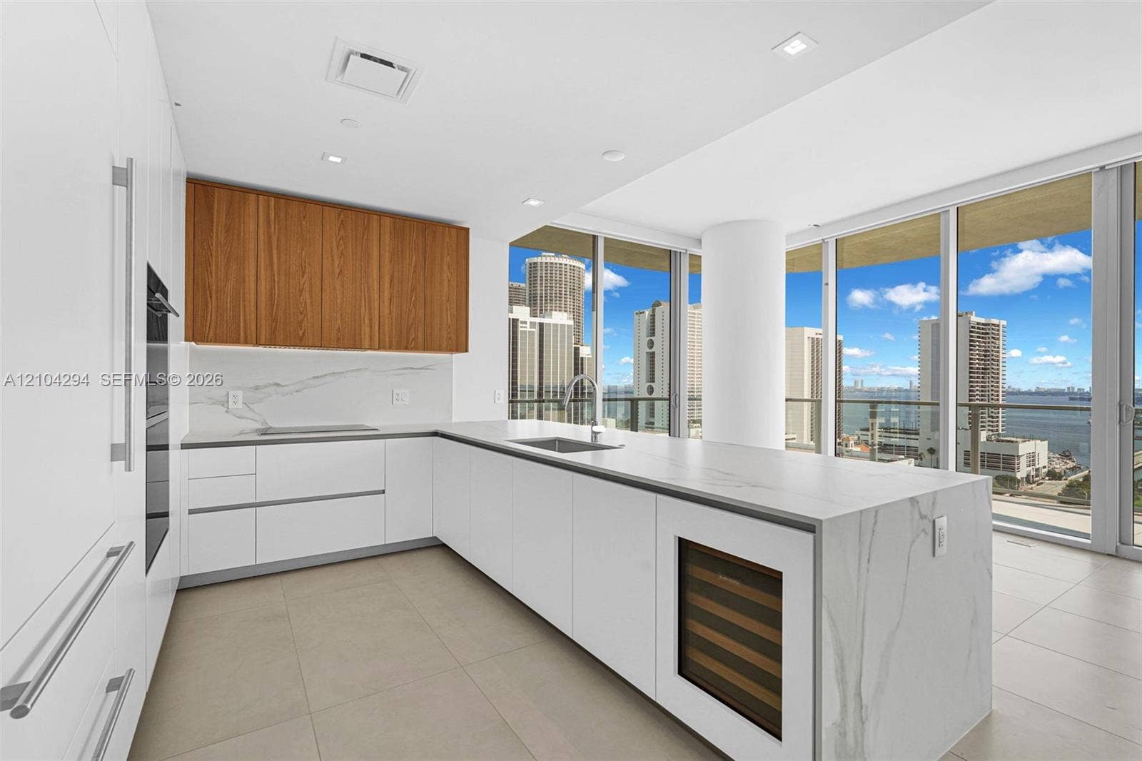 1400 Biscayne Boulevard, #1606, Miami, FL 33132 Sleek kitchen featuring white cabinetry, wood-finish upper cabinets, integrated stainless steel appliances, and a central island with a built-in wine refrigerator
