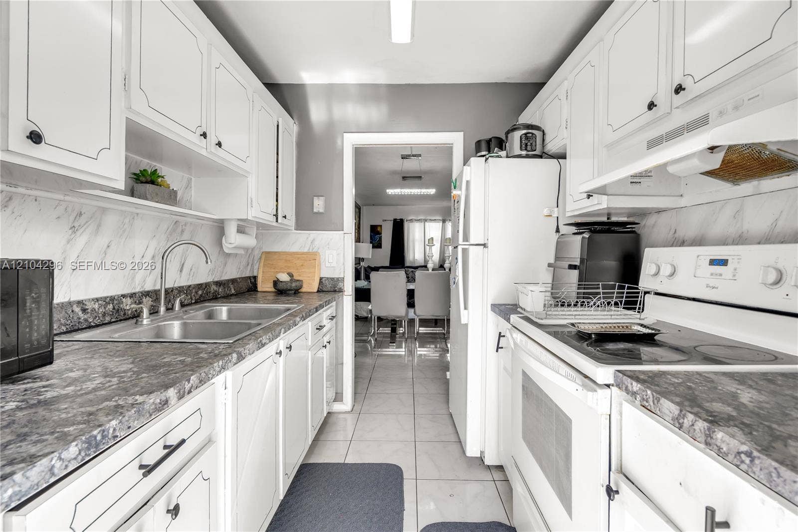 Kitchen featuring white cabinetry, stone-patterned laminate countertops, marble-patterned backsplash, stainless steel dual-basin sink, and ceramic tile flooring