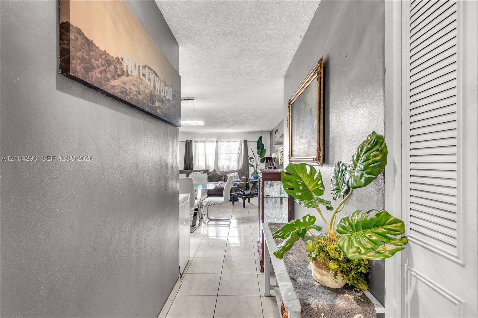 Interior hallway featuring light-colored tile flooring, smooth neutral-tone walls, and a white louvered closet door