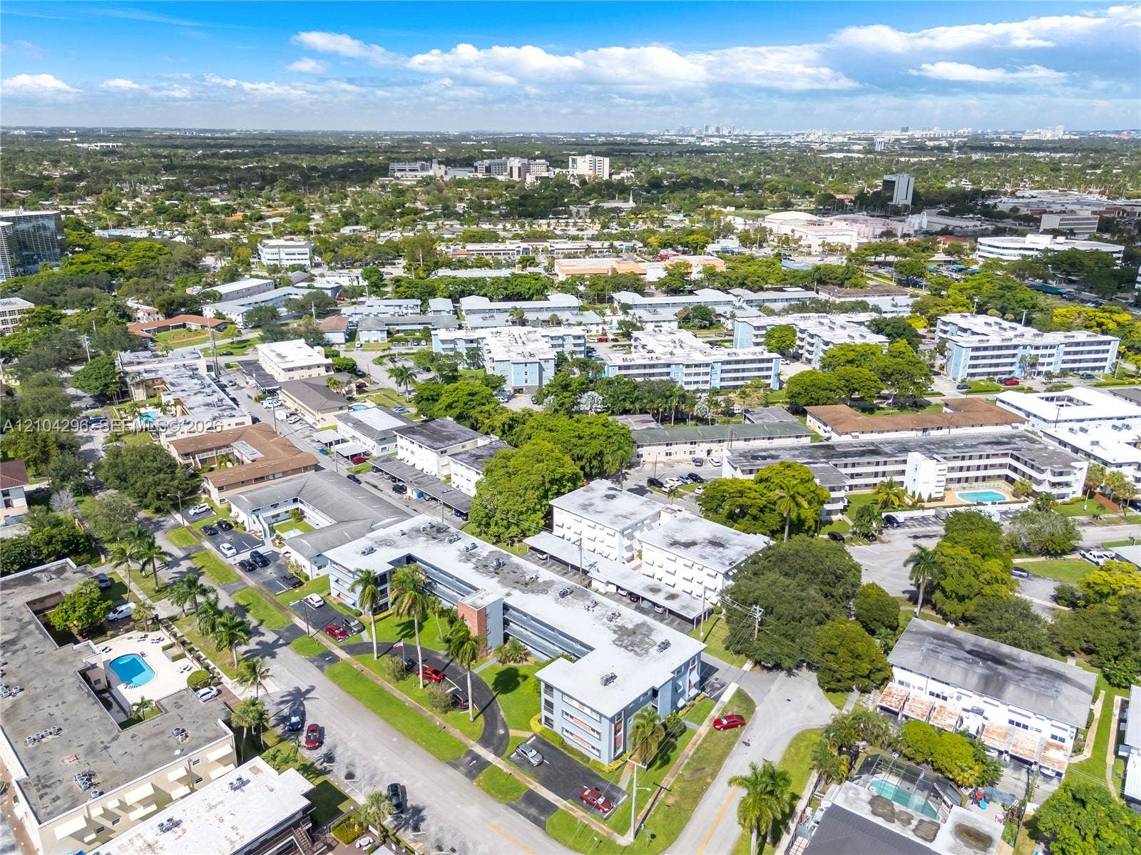 Aerial perspective of a multi-building residential complex featuring mature landscaping, paved parking areas, and exterior swimming pools