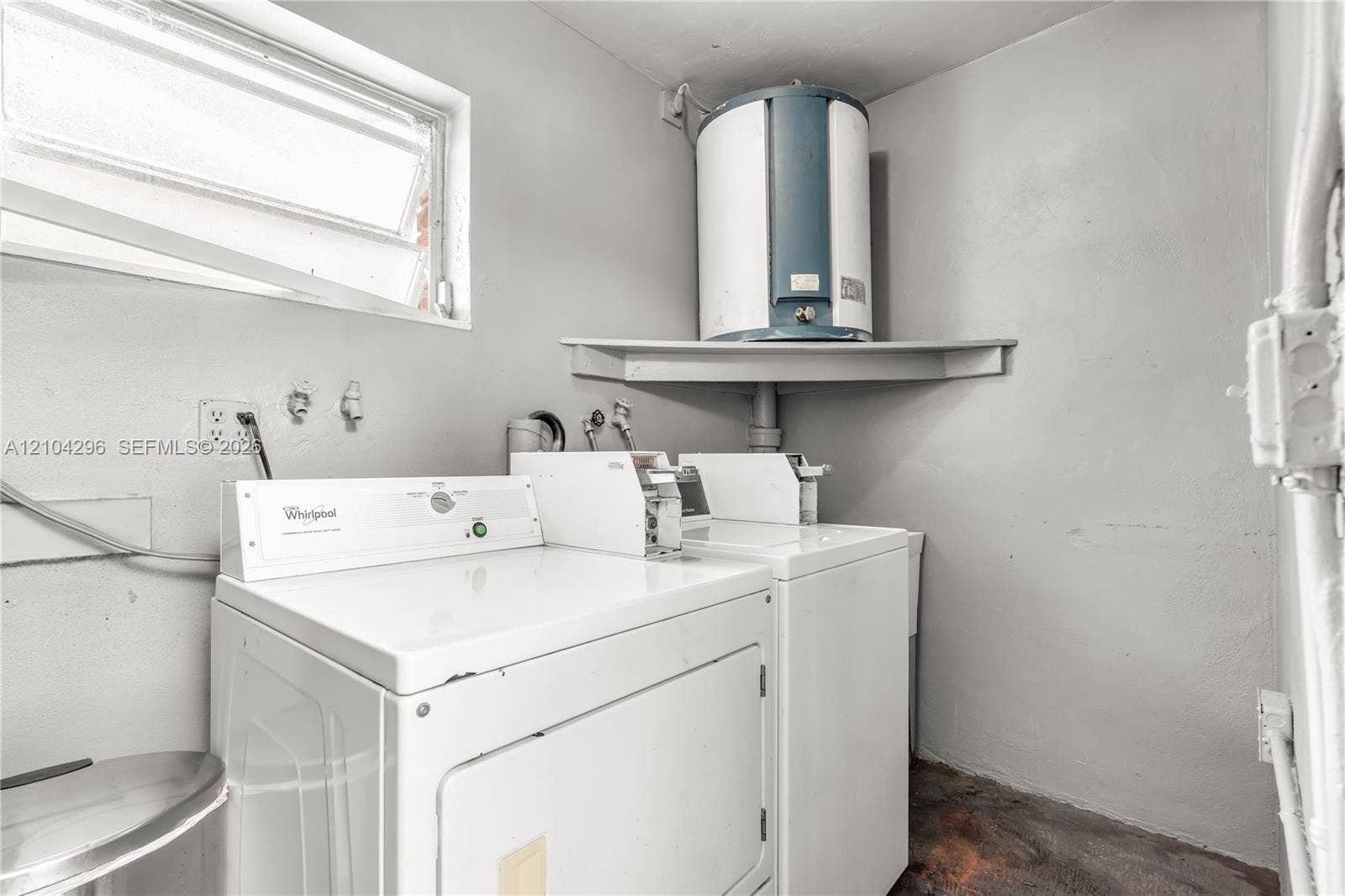 Utility space featuring an elevated water heater, wall-mounted shelving, laundry hookups, and a hopper-style window