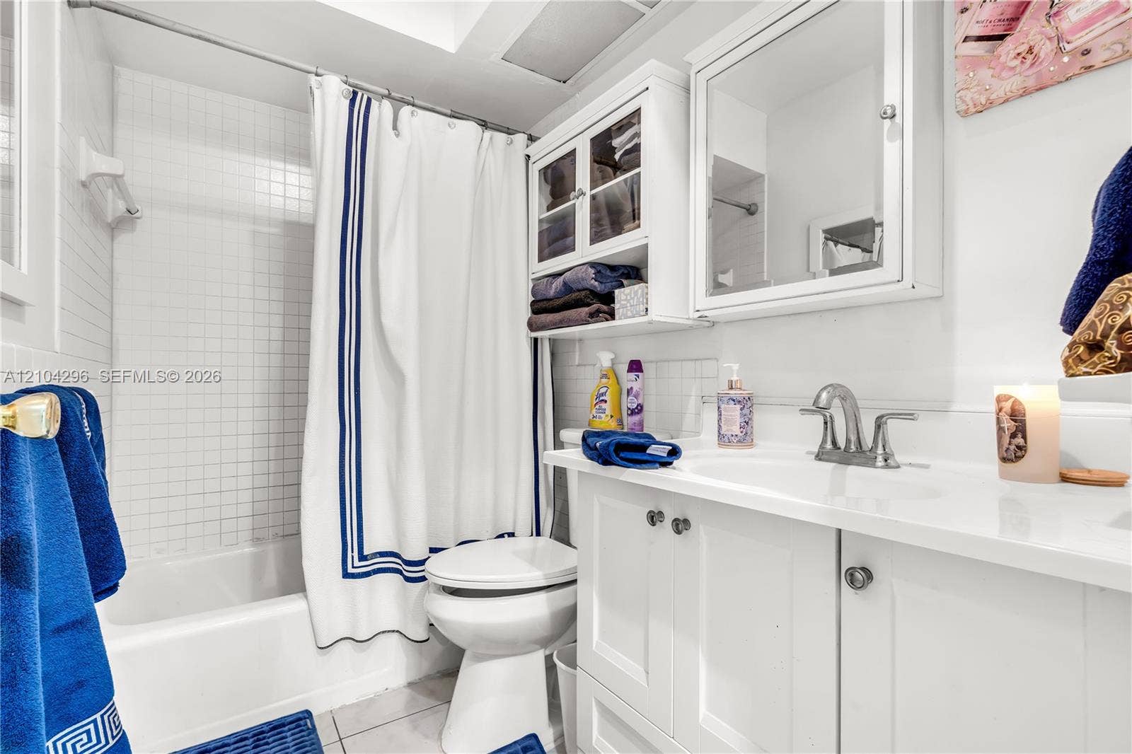 Bathroom featuring a white vanity cabinet with an integrated sink, polished metal faucet, built-in medicine cabinet with shelving, and a tiled shower surround