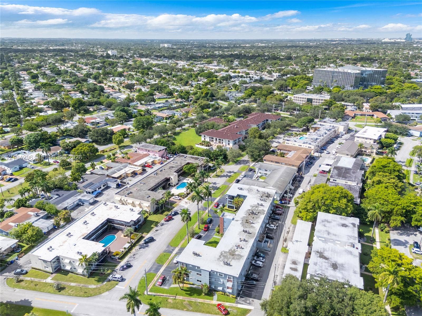 Aerial perspective of a multi-unit residential complex featuring flat-roof structures, dedicated parking areas, and a communal swimming pool