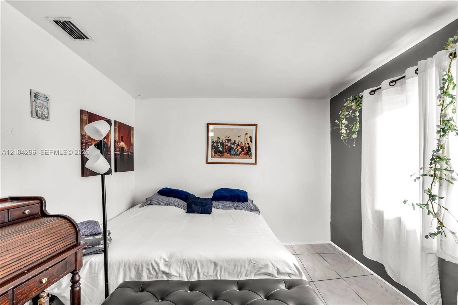 Neutral-toned room featuring large-format ceramic tile flooring, a high-contrast charcoal accent wall, and a large window with white curtains