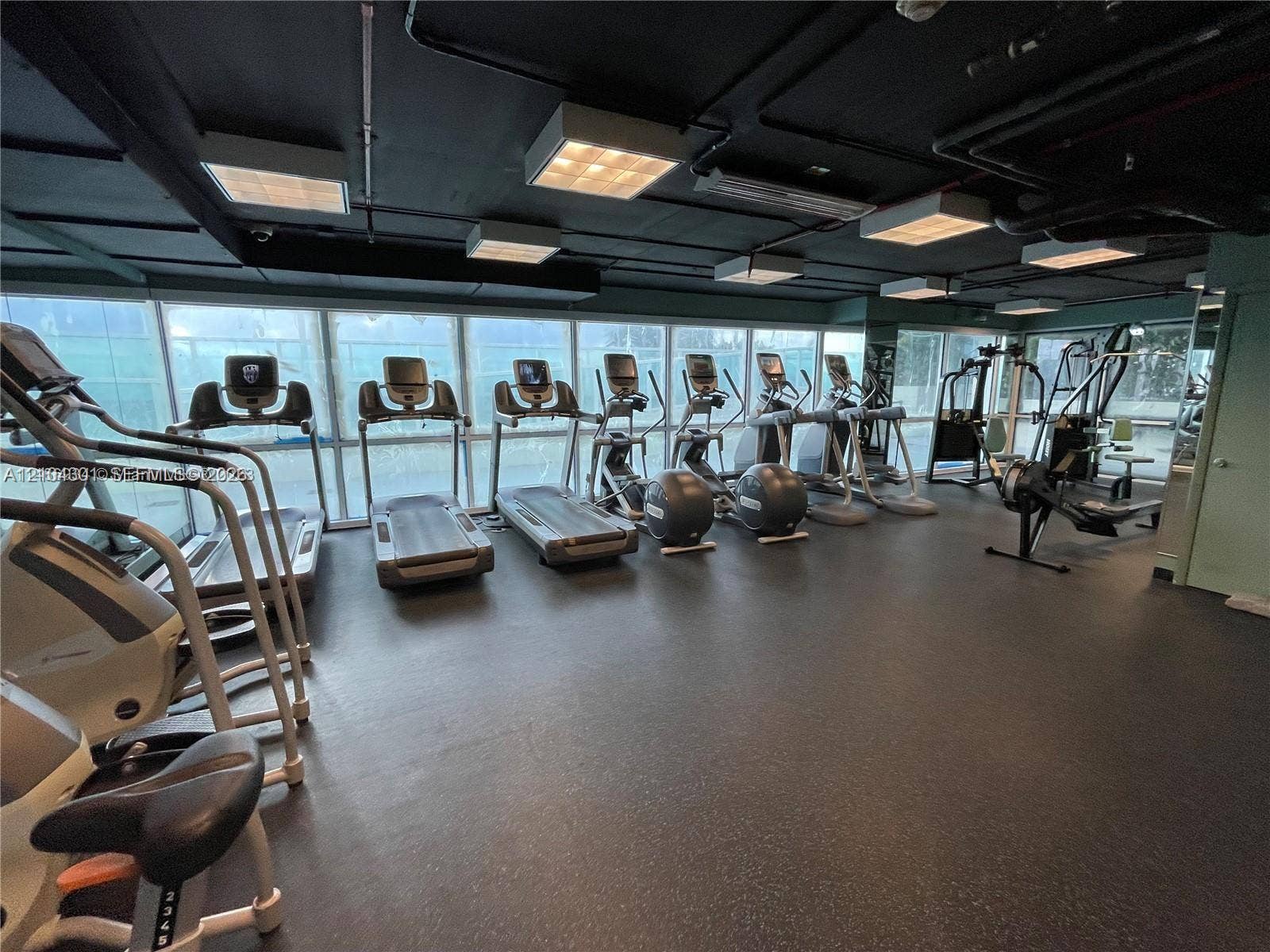 Fitness center featuring expansive floor-to-ceiling windows, industrial-style exposed ceiling, and specialized rubberized flooring