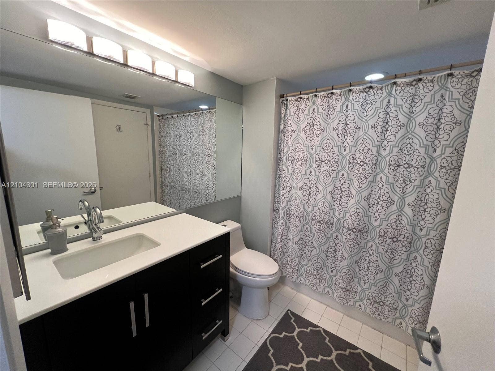 Dark wood-finish vanity with rectangular integrated sink, white composite countertop, polished chrome faucet, full-width vanity mirror, and linear light fixture