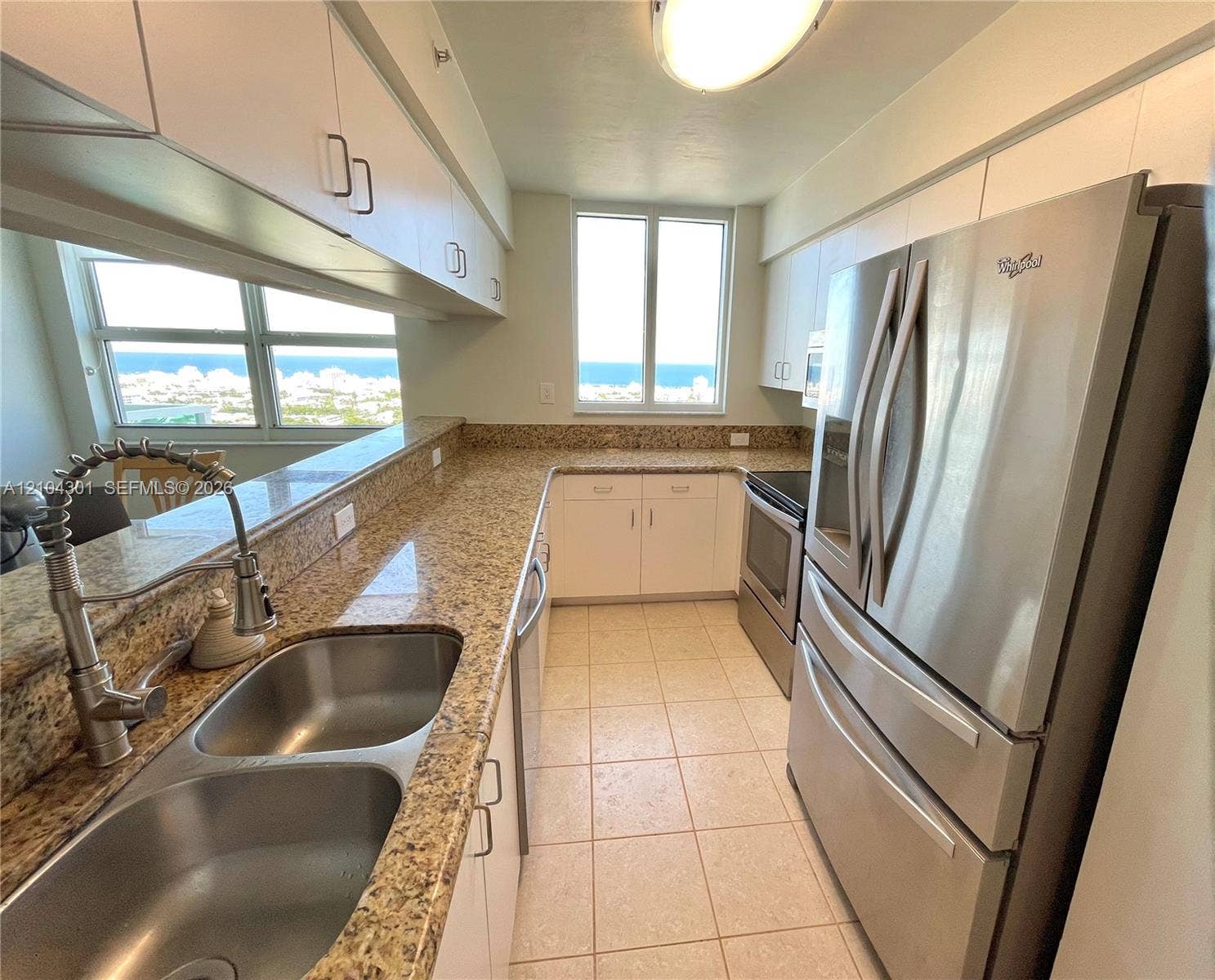 Kitchen featuring stainless steel appliances, stone-finish countertops, dual-basin under-mount sink with pull-down faucet, white cabinetry, and ceramic tile flooring