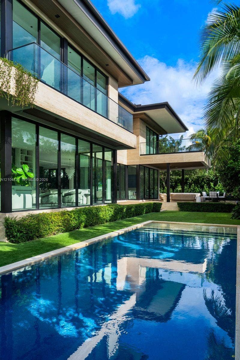 Contemporary multi-level exterior featuring floor-to-ceiling glass walls, sleek glass balcony railings, stone-finish cladding, and a private swimming pool with integrated hardscaping