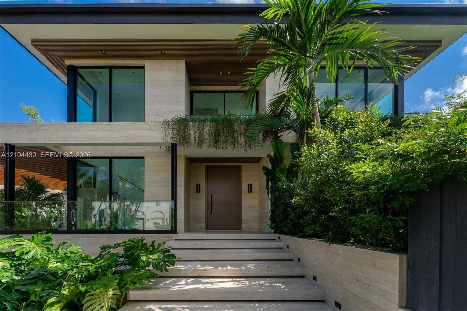 Modern two-story architectural exterior featuring stone tile cladding, wide-plank wood-finish soffits, expansive glass sliding doors, and a glass-paneled staircase railing