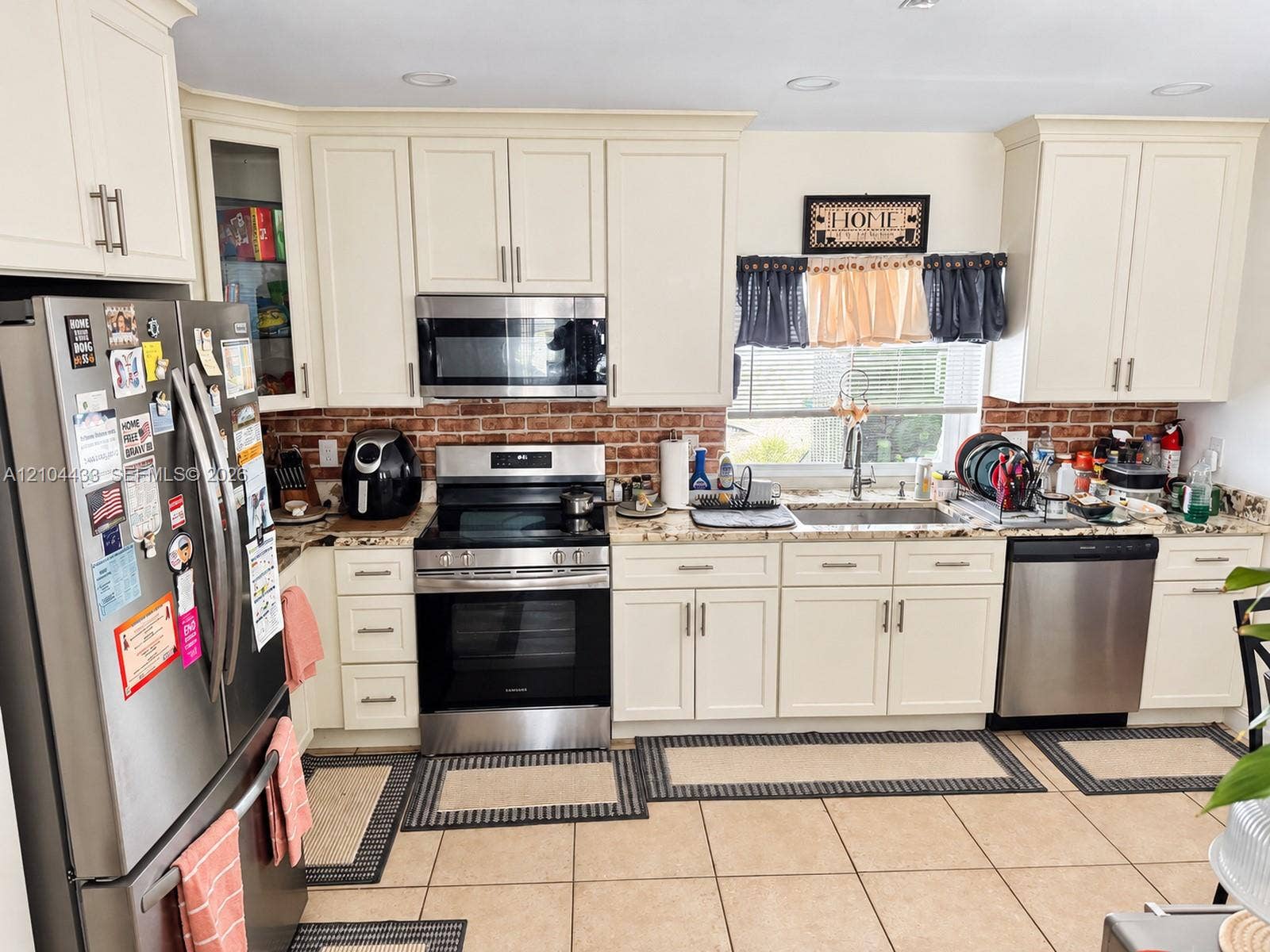 7380 NW 9th Street, Plantation, FL 33317 Cream-colored cabinetry with brushed nickel hardware, stainless steel appliances, brick-patterned tile backsplash, granite-style countertops, and tile flooring