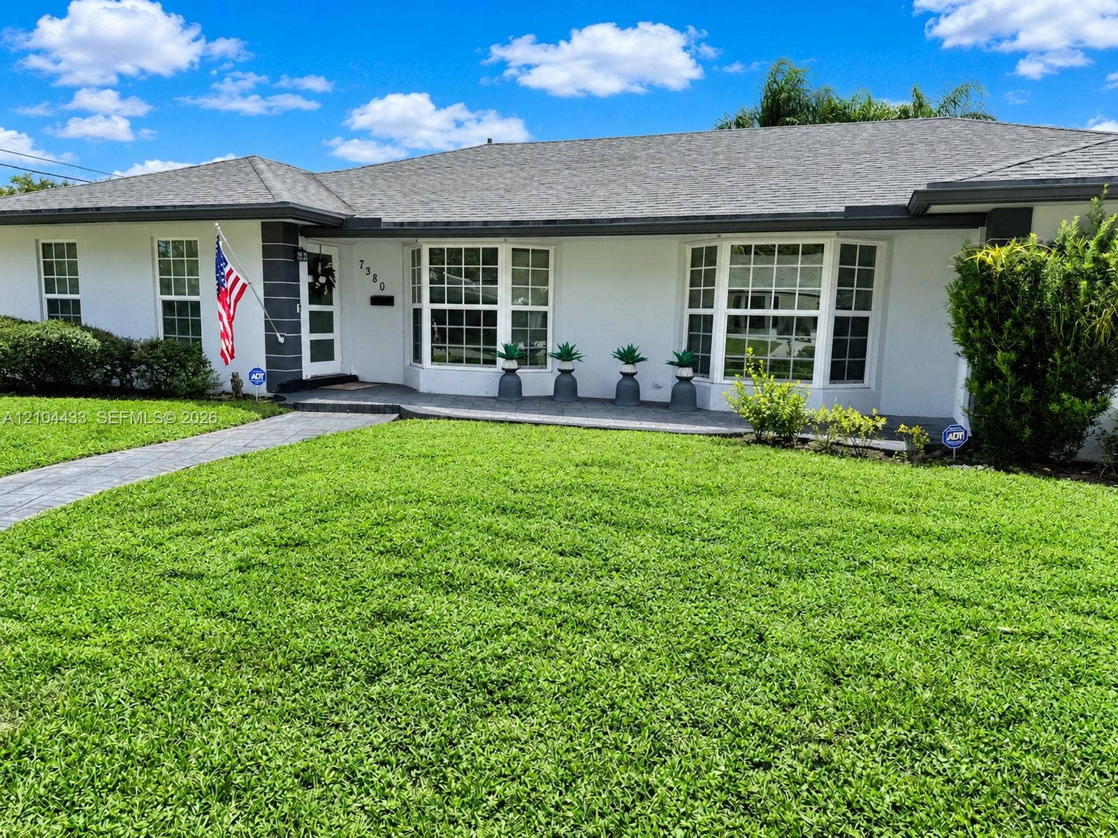 7380 NW 9th Street, Plantation, FL 33317 Smooth stucco exterior with a gray shingle roof, a patterned walkway, and established landscaping