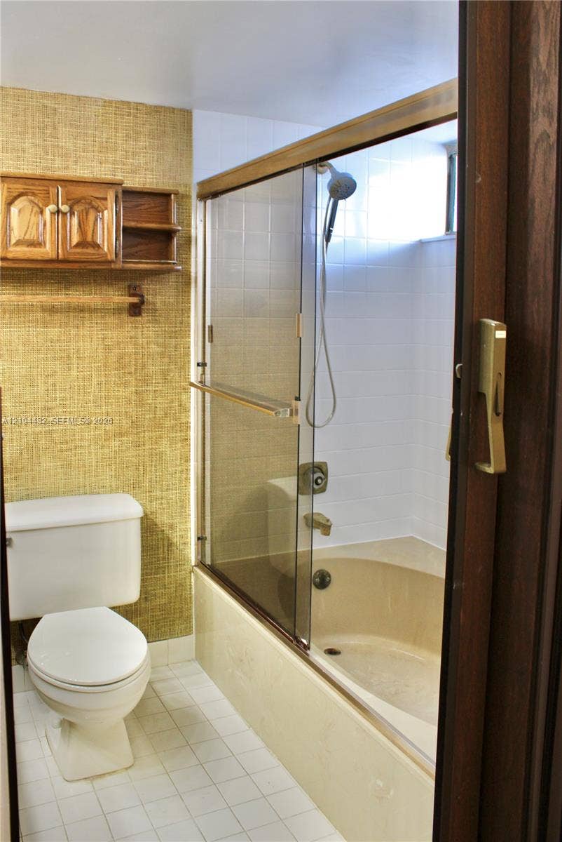 18000 NW 68th Avenue, #409A, Hialeah, Hialeah, FL 33015 Bathroom featuring a tub-shower combination with glass sliding doors, white tile surround, built-in wooden cabinetry, and textured wall finish