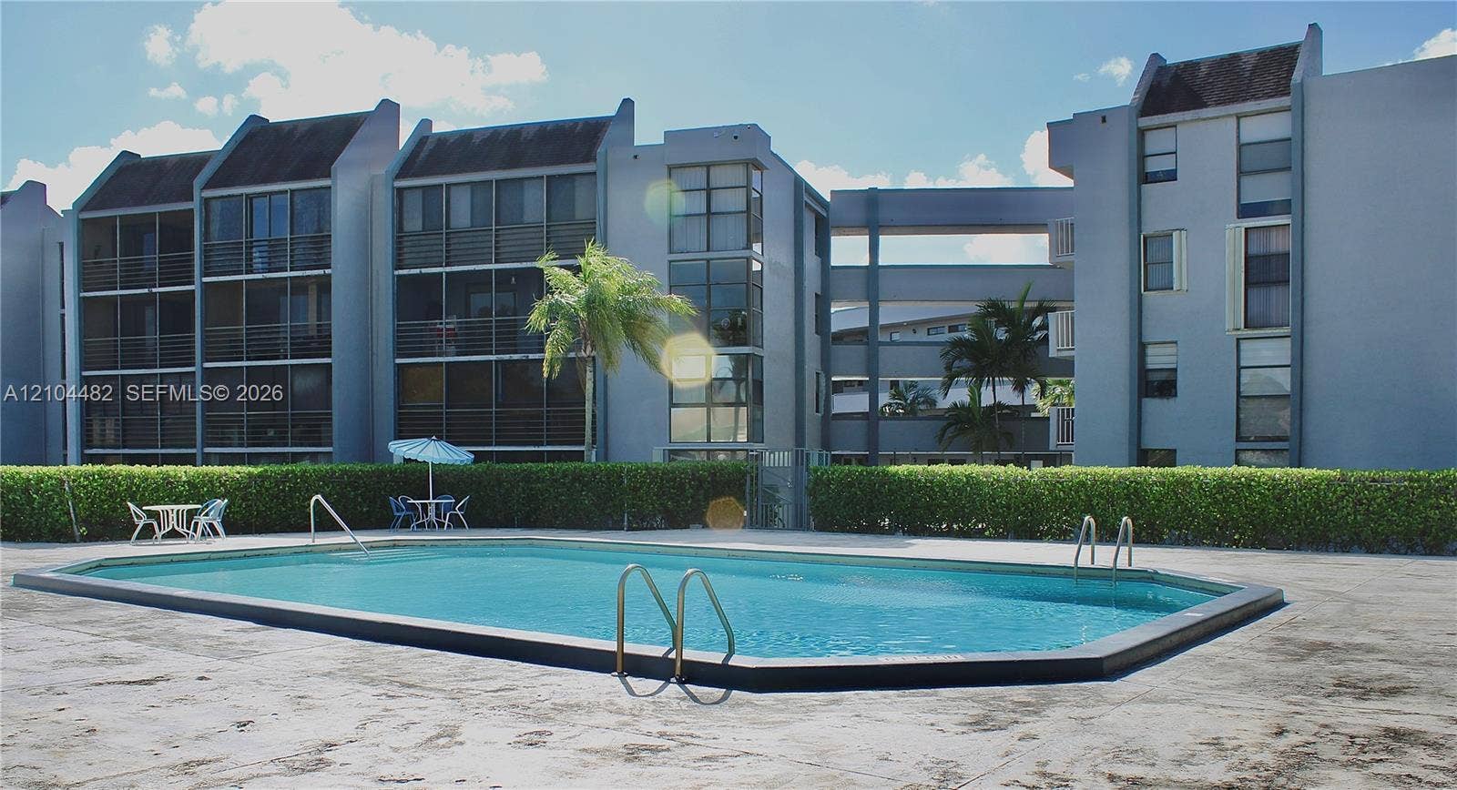 18000 NW 68th Avenue, #409A, Hialeah, Hialeah, FL 33015 Rectangular swimming pool featuring a concrete deck, metal handrails, and a surrounding privacy hedge