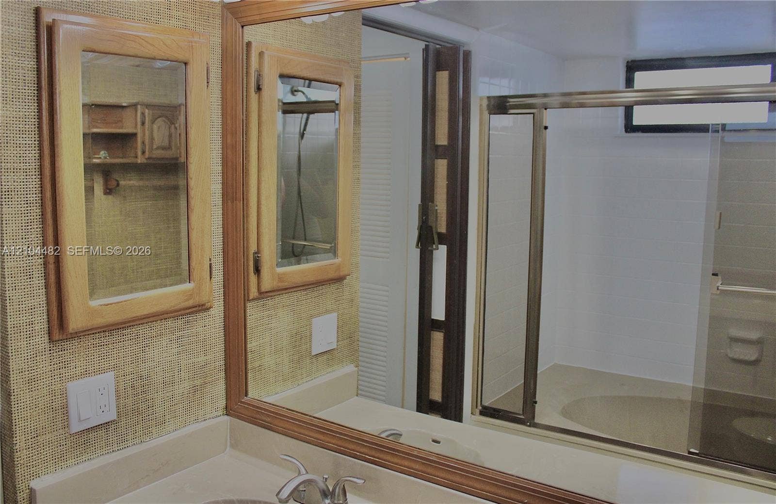 18000 NW 68th Avenue, #409A, Hialeah, Hialeah, FL 33015 Bathroom featuring dual wood-framed medicine cabinets, a large wall-mounted mirror, a neutral-toned integrated sink vanity, and a sliding glass-door shower enclosure