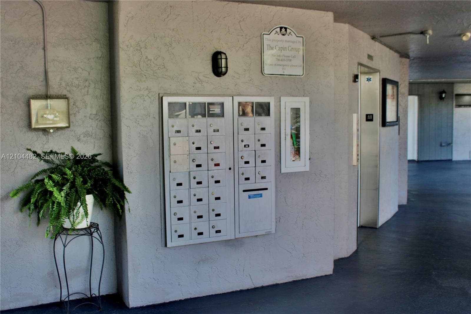 18000 NW 68th Avenue, #409A, Hialeah, Hialeah, FL 33015 Stucco exterior hallway featuring a centralized metal mail station, integrated fire extinguisher cabinet, and elevator access