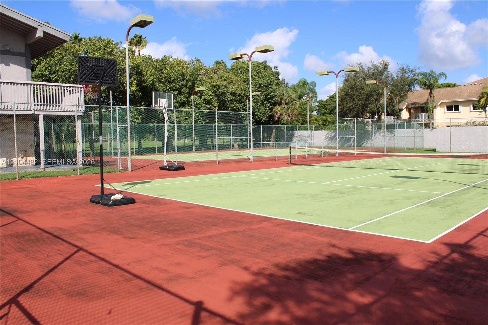 18000 NW 68th Avenue, #409A, Hialeah, Hialeah, FL 33015 Multi-purpose sports court featuring a tennis surface, basketball hoop, perimeter chain-link fencing, and overhead court lighting