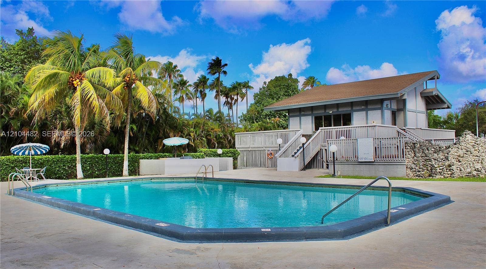 18000 NW 68th Avenue, #409A, Hialeah, Hialeah, FL 33015 In-ground swimming pool with a concrete deck, built-in stone-accented wall, and exterior structure featuring a second-level deck with wooden staircase