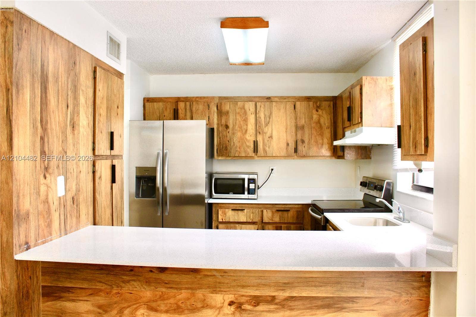 18000 NW 68th Avenue, #409A, Hialeah, Hialeah, FL 33015 Kitchen featuringwhite solid-surface countertops, a stainless steel refrigerator, an integrated microwave, and an undermount sink