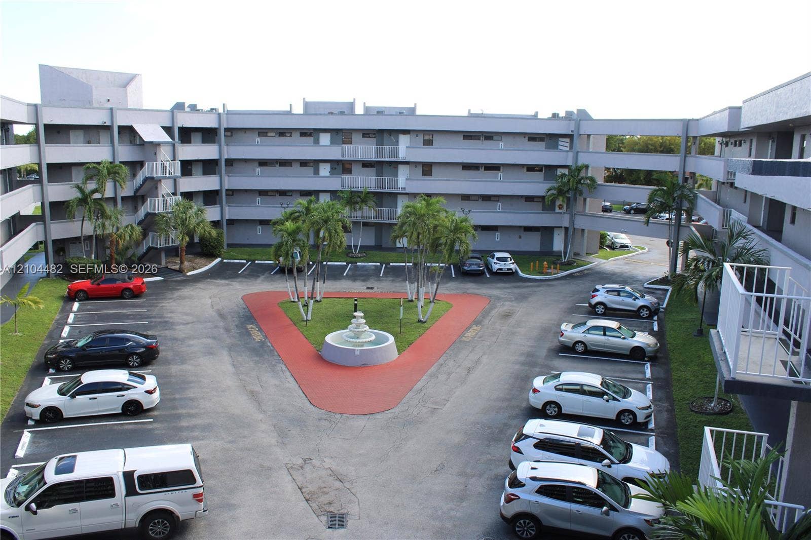 18000 NW 68th Avenue, #409A, Hialeah, Hialeah, FL 33015 Multi-level exterior architecture featuring open-air walkways, a central courtyard with a decorative fountain, and lush palm landscaping