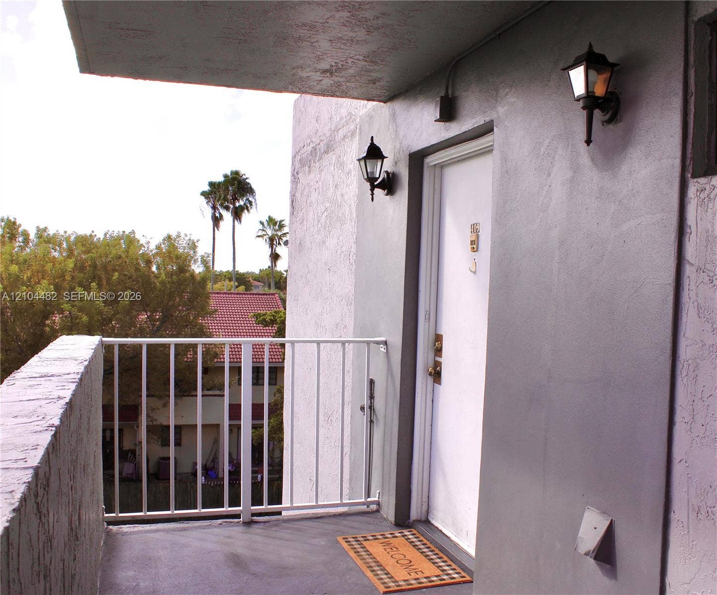 18000 NW 68th Avenue, #409A, Hialeah, Hialeah, FL 33015 Covered balcony entryway featuring a painted concrete surface, white metal railings, and dual wall-mounted exterior lanterns