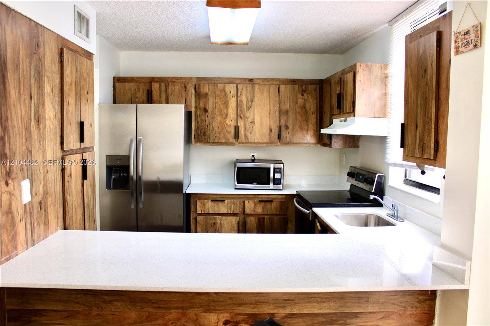 18000 NW 68th Avenue, #409A, Hialeah, Hialeah, FL 33015 Kitchen featuring wood-finish cabinetry, white solid-surface countertops, a breakfast bar, and stainless steel appliances