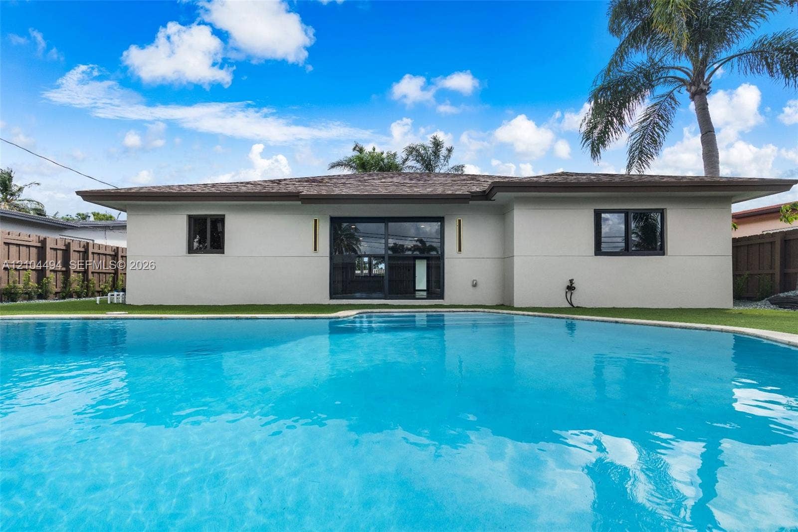 711 NW 8th Avenue, Dania Beach, FL 33004 In-ground swimming pool, exterior sliding glass doors, horizontal wood privacy fencing, and neutral-toned stucco siding