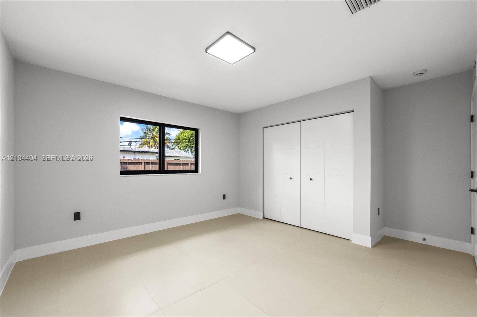 711 NW 8th Avenue, Dania Beach, FL 33004 Neutral-toned room featuring large-format tile flooring, a square flush-mount LED fixture, a black-framed window, and a built-in closet with double doors