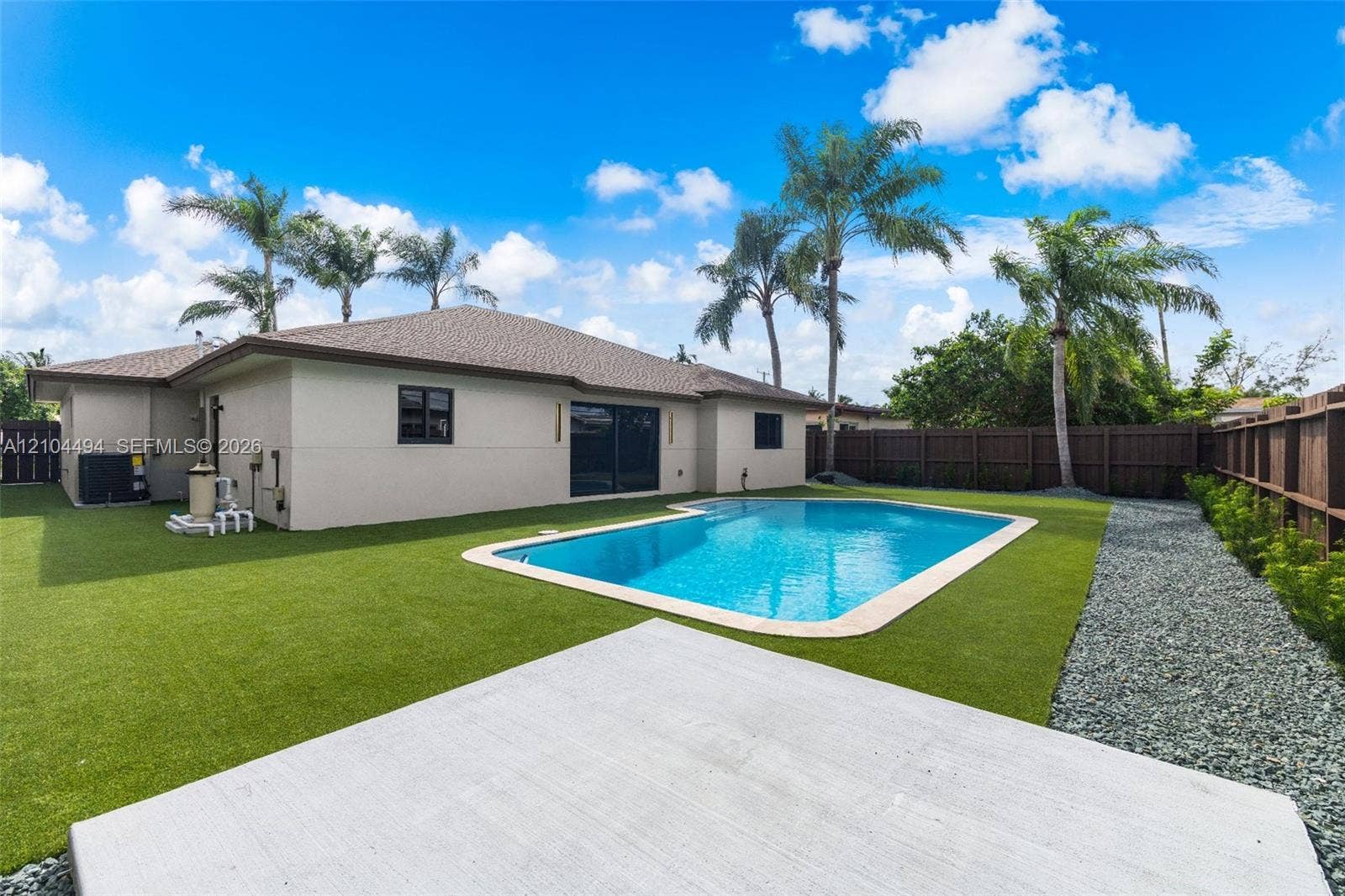 711 NW 8th Avenue, Dania Beach, FL 33004 Backyard featuring an in-ground swimming pool, synthetic turf lawn, concrete patio, privacy fencing, and palm trees