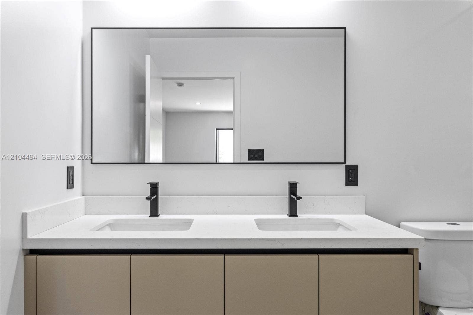 711 NW 8th Avenue, Dania Beach, FL 33004 Double vanity featuring solid-surface countertop, dual rectangular undermount sinks, matte black widespread faucets, flat-panel cabinetry, and a large rectangular mirror with a thin black frame