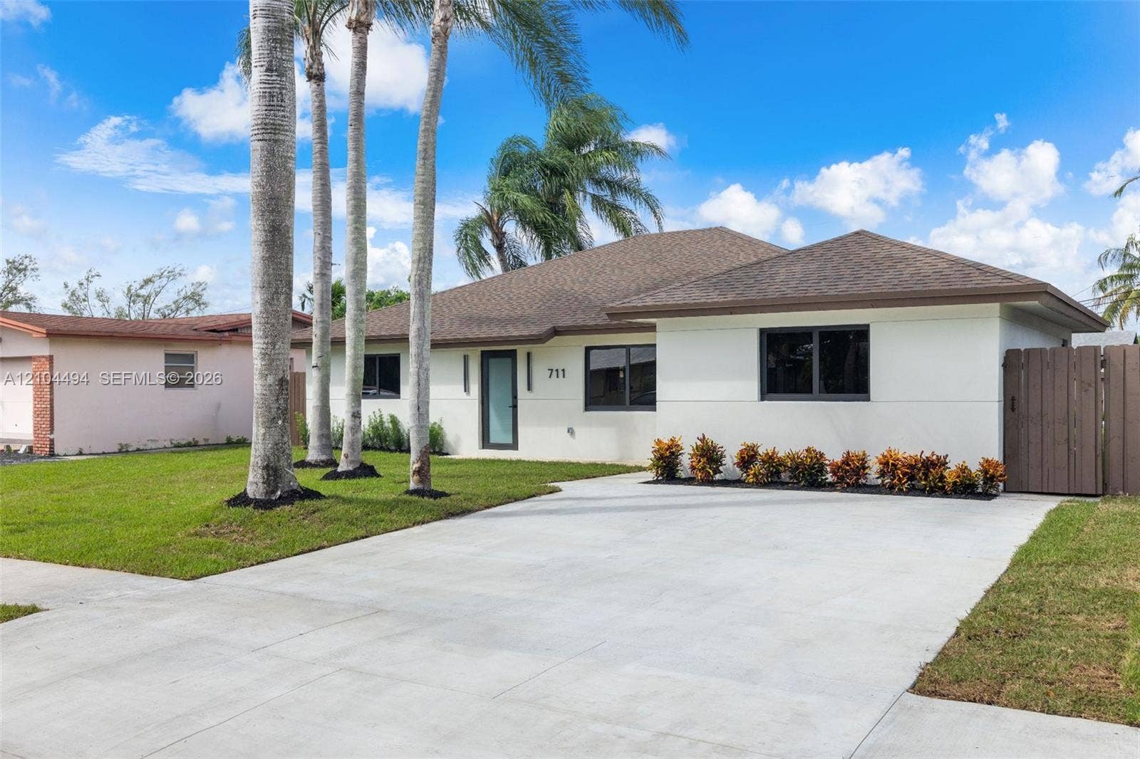 711 NW 8th Avenue, Dania Beach, FL 33004 Single-story residence featuring a neutral stucco exterior, a concrete driveway, modern dark-framed windows, and a privacy fence