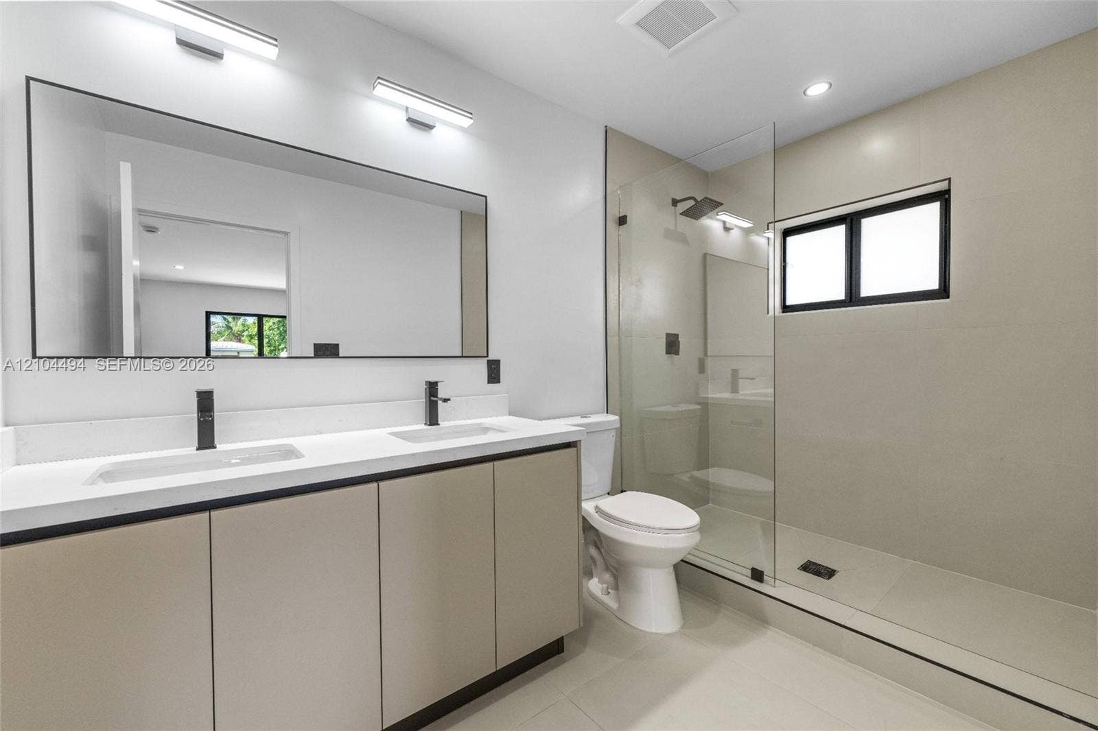 711 NW 8th Avenue, Dania Beach, FL 33004 Dual-sink vanity with light-tone cabinetry and white countertop, large wall-mounted mirror, walk-in glass-enclosed shower, and matte black plumbing fixtures