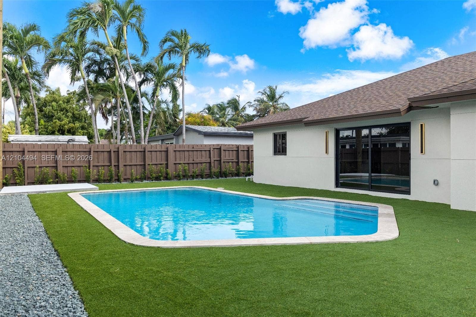 711 NW 8th Avenue, Dania Beach, FL 33004 In-ground swimming pool with integrated stairs, low-maintenance artificial turf, privacy fencing, and exterior wall-mounted lighting