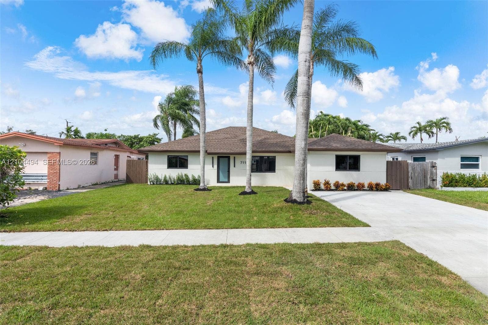 711 NW 8th Avenue, Dania Beach, FL 33004 Single-story exterior featuring a shingled roof, stucco finish, concrete driveway, and mature palm trees